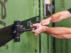 Two arms tightly roll out sheathing tape on a wall to the left.