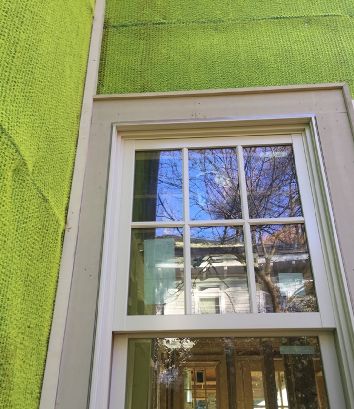 An exposed green mesh vented rain screen surrounds a window on a house.