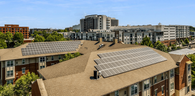 Solar panels on top of a roof of a multifamily housing complex with city skyline in the background.